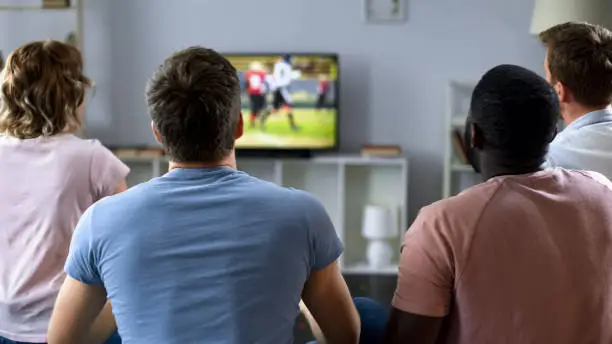 Group of multiethnic friends supporting football team, watching match on tv