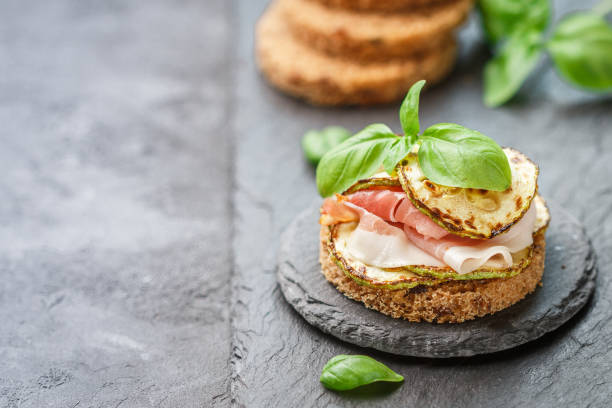 istock Mini ham  (hamon, prosciutto) sandwiches, fried zucchini and Basil close-up on black surface. Gourmet snack 982019972