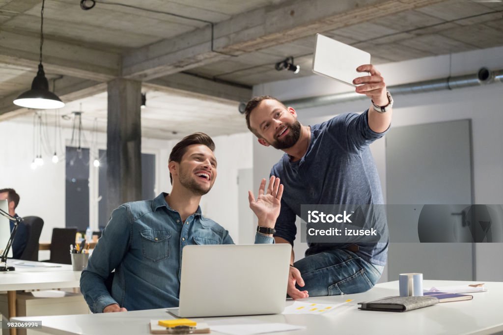 Creative business men taking a selfie with digital tablet Two creative business men taking a selfie with digital tablet in office. Business people in office taking self portrait with digital tablet. Adult Stock Photo