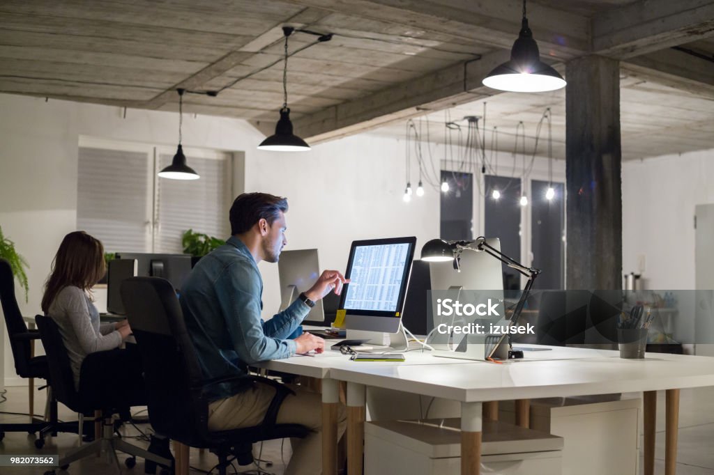 Businesspeople working in modern office Young man working at his desk with female colleague in background. Businesspeople working in modern office. Adult Stock Photo