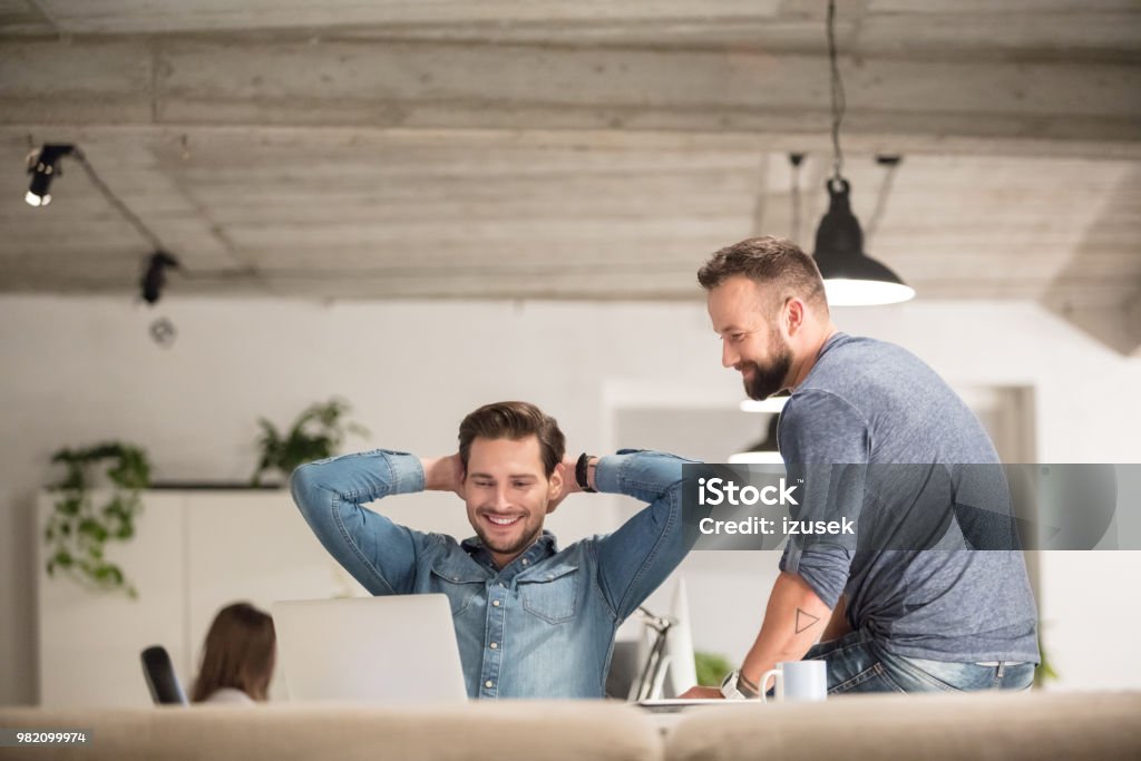 Creative professionals working in office Two relaxed men looking at laptop in office. Creative professionals working on laptop and smiling. Adult Stock Photo