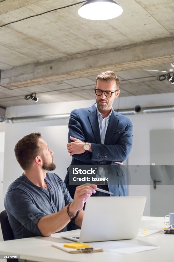 Businessman discussing over new project in office Two businessman discussing over new project in office. Man sitting at his desk talking with manager. Adult Stock Photo