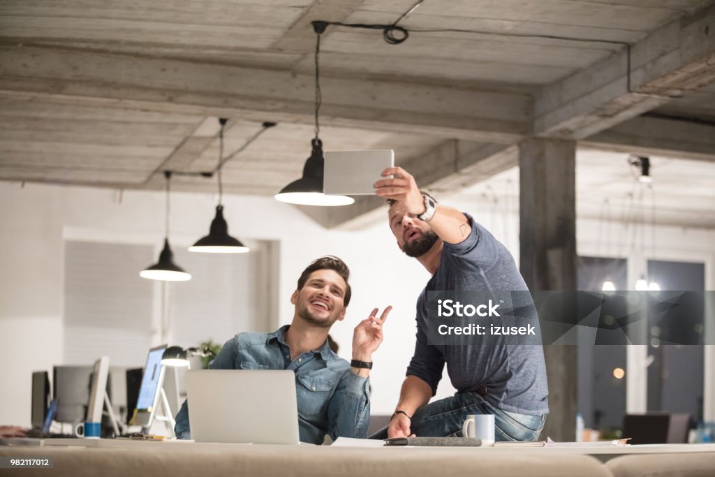 Businessmen taking a selfie in office Two creative businessmen taking a selfie with digital tablet in office. Business people in office taking self portrait with digital tablet. Symbols Of Peace Stock Photo