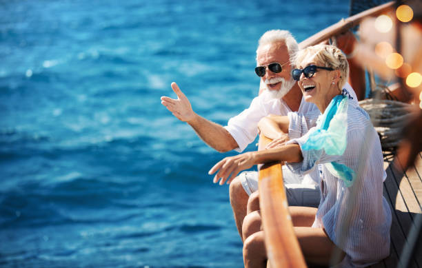 Senior couple on a sailing cruise. Closeup side view of mid 60's couple enjoying a sailing cruise during  summer vacation at seaside. old boat stock pictures, royalty-free photos & images