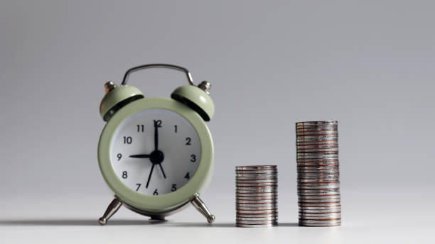 istock Two piles of coins that are different in height from the alarm clock. 982201544