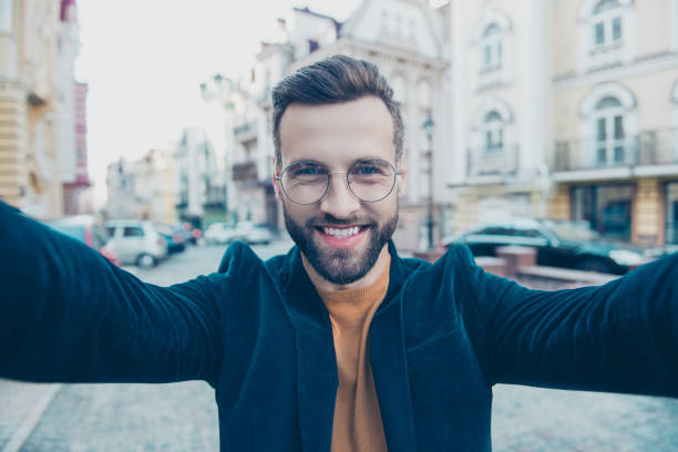 istock Portrait of cheerful attractive man shooting selfie on front camera with two hands while walking over street background. Tourism tourist travel traveler concept 982223972