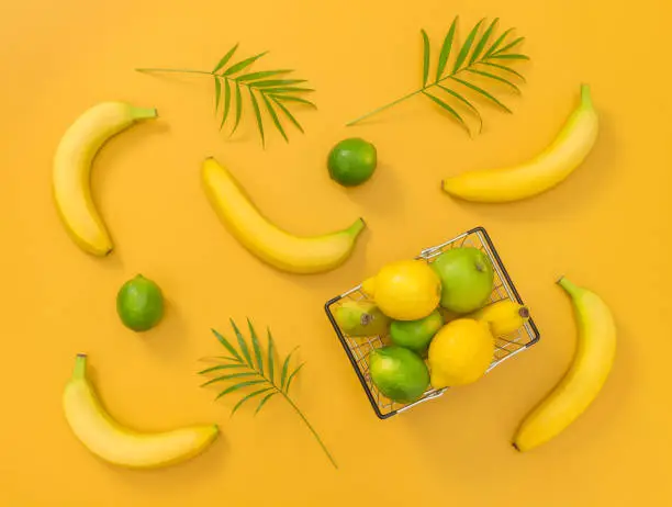Bananas, limes, lemons and palm leaves on bright yellow background. Tropical summer theme.