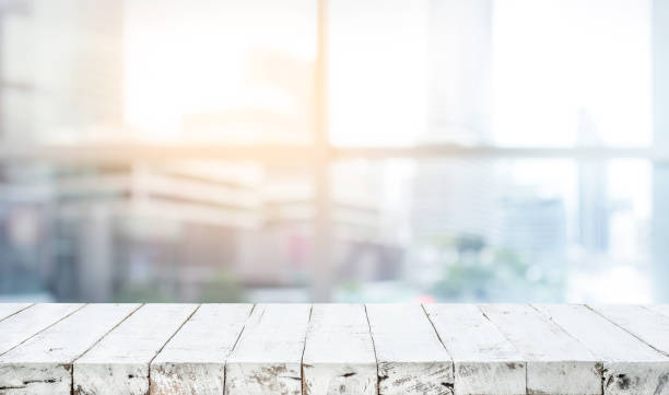 istock Wood table top on blur white glass window background form office building 982239362