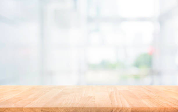 istock Wood table top on blur white glass wall background form office building 982239384