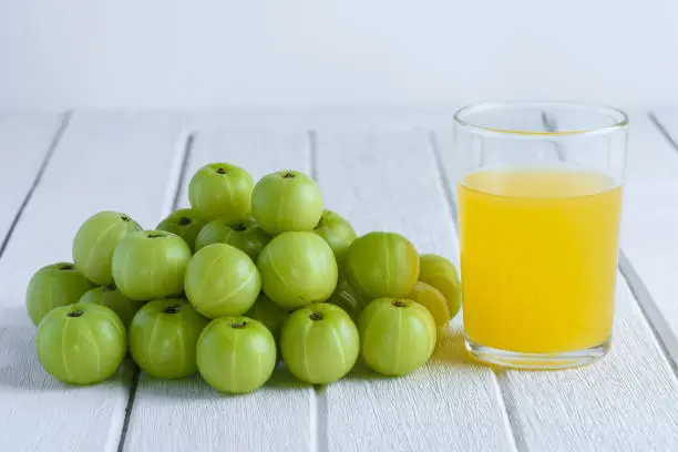 Indian gooseberry and juice on white wooden table