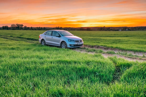 Summer landscape at sunset with Volkswagen Polo Vento car Dobrush, Belarus - May 27, 2017: Volkswagen Polo Vento car in green grass on a rural road at the background of an orange sunset sky in summer car-on-city-road-side-view stock pictures, royalty-free photos & images