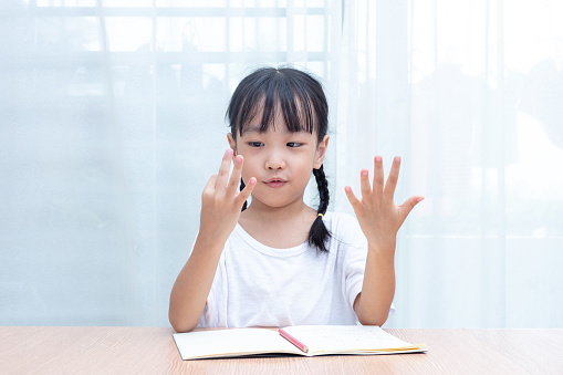 Asian little Chinese Girl doing mathematics by counting fingers at home