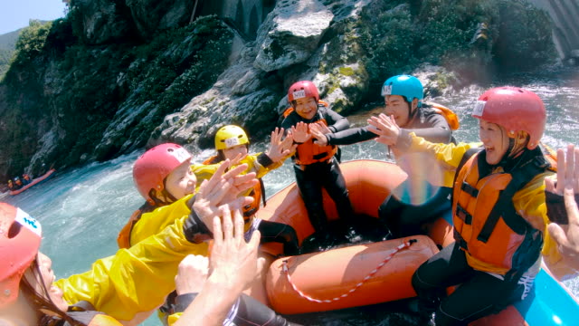 Personal point of view of a group of people with their paddles in the air celebrating success while white water river rafting