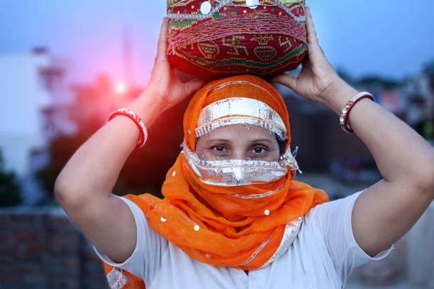 Portrait of a traditional mature Indian woman carrying a water pot on her head and looking at camera.