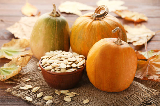 istock Orange pumpkins with dry leafs and seeds on wooden table 982359878