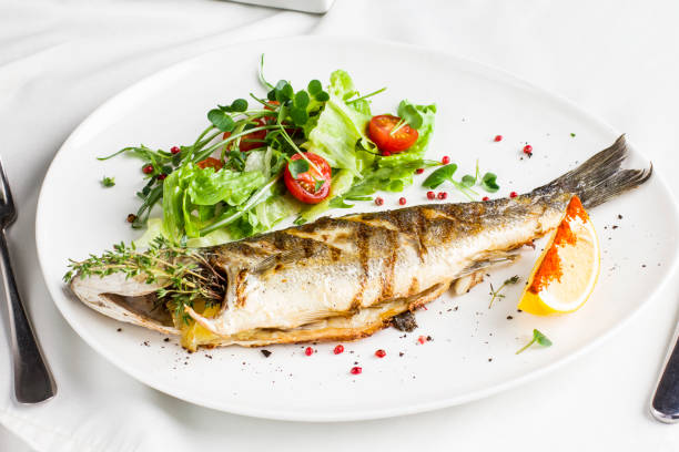 istock Baked fish with lemon and fresh vegetables on a white plate in the restaurant 982374482