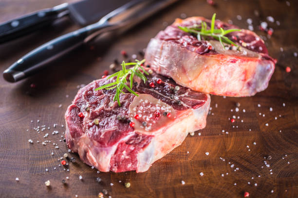 istock Two raw pieces beef shank on wooden butcher board with fork and knife 982379064