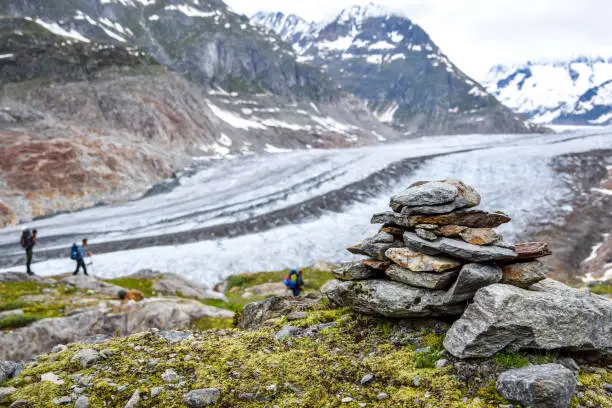 Stunning view of Aletsch glacier, the largest glacier in the European Alps, located in the Bernese Alps in Switzerland. A Stoneman (rock cairn) in the foreground. Unrecognizable hikers in background.