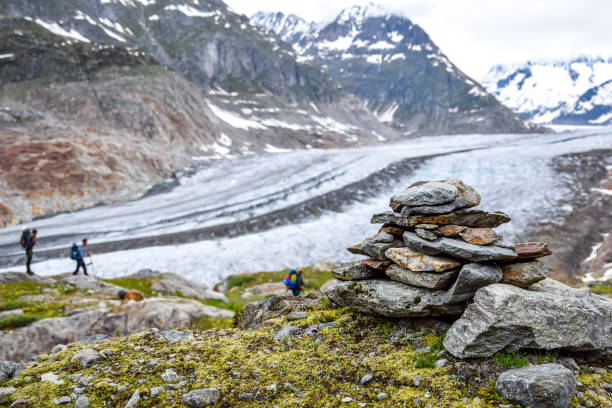 stunning view of aletsch glacier, the largest glacier in the european alps, located in the bernese alps in switzerland. a stoneman (rock cairn) in the foreground. unrecognizable hikers in background. - switzerland cold green rock imagens e fotografias de stock