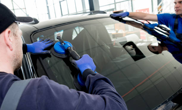Automobile special workers replacing windscreen or windshield of a car in auto service station garage. Automobile special workers replacing windscreen or windshield of a car in auto service station garage. Background replacement stock pictures, royalty-free photos & images