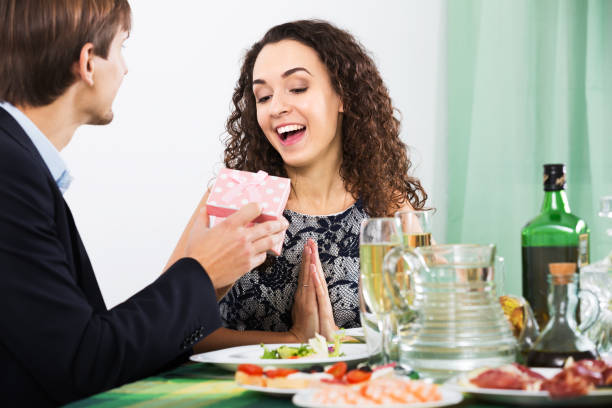 Man giving present to woman Man giving present to woman during romantic dinner with champagne in home wonderingly stock pictures, royalty-free photos & images