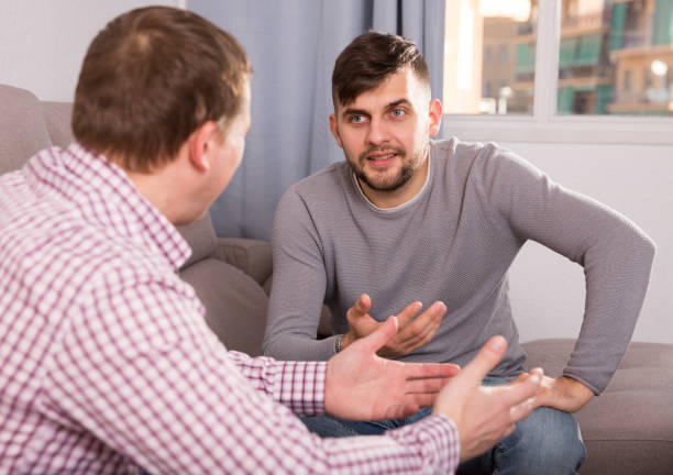 istock Cheerful man talking with friend on sofa 982388146