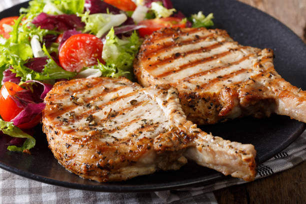 Grilled pork steak with bone and fresh salad close-up. horizontal Grilled pork steak with bone and fresh salad close-up on a plate. horizontal pork stock pictures, royalty-free photos & images