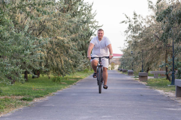 A fat man rides a bicycle along the mall during the day A fat man rides a bicycle along the mall overweight boy stock pictures, royalty-free photos & images