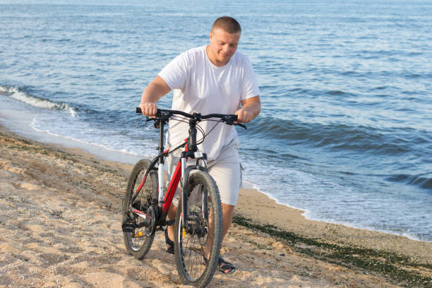 A fat man drives a bicycle along the seashore