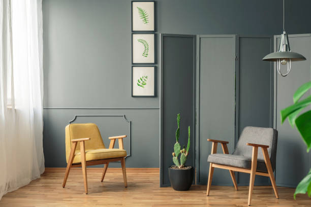 istock Two chair standing in a grey room interior with hanging lamp, next to a screen and a cactus 982402144