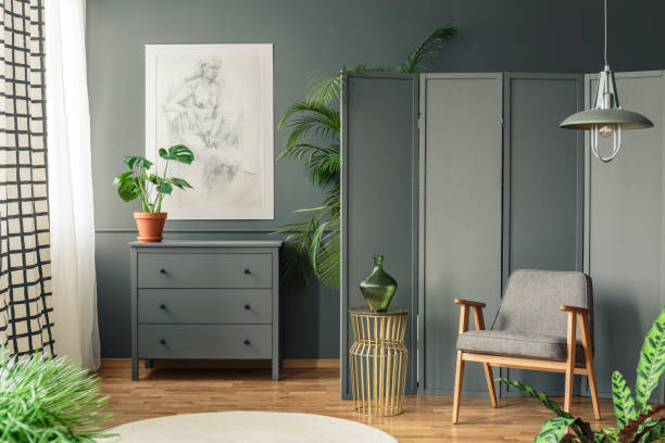 istock Grey chair with a decorative screen standing next to a shelf surrounded by plants in a grey, botanic room interior 982402162