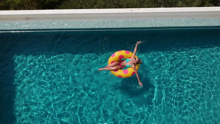 Aerial view video of a woman relaxing on a inflatable ring and floating in the pool