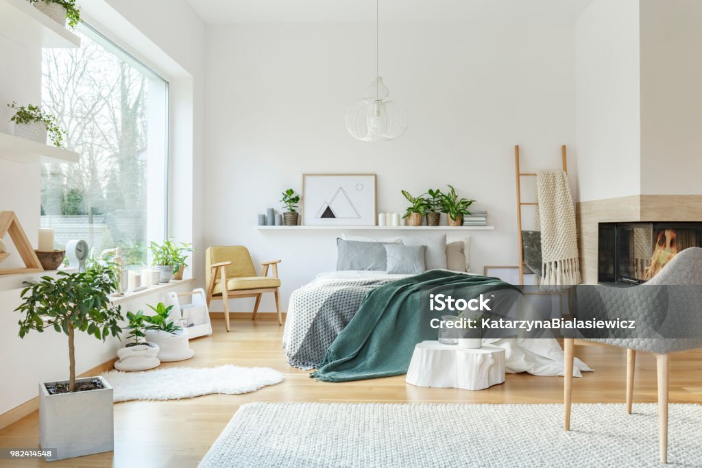 Green and yellow bedroom interior Poster and plants on shelf above bed in green and yellow bedroom interior with armchair Bedroom Stock Photo