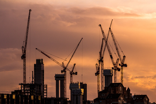 Color image depicting cranes and heavy duty construction equipment on the London skyline as the sun sets. The cranes have been busy constructing blocks of flats and apartments to ease the housing crisis in London and the south east of England. Lots of room for copy space.