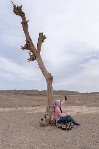 girl under wilt tree taking selfie photo on gobi desert