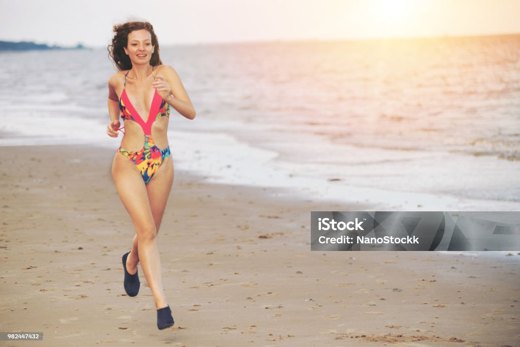 Attractive woman runs on sand beach in summer. Attractive woman runner runs on tropical sand beach in summer. Healthy lifestyle and running sport concept. Marathon Stock Photo