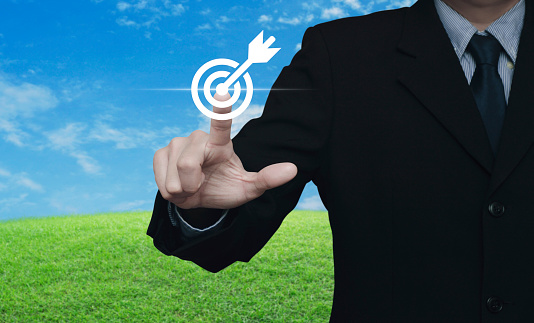 Businessman pressing target with dart icon over green grass field with blue sky, Business success concept