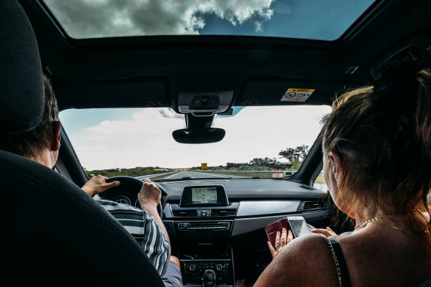 車の助手席に古いカップル。道路の旅行のコンセプトです。女性は、ドライブ間の男性暇つぶしにスマート フォンを使用してください。 - car driving inside of indoors ストックフォトと画像