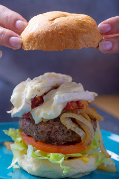 istock A bread bun is placed onto a  being prepared cheese and bacon burger 982504016
