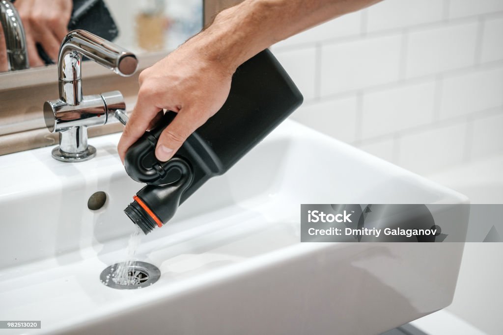 Removal of blockage in the sink, the hand of a man with a bottle of a special remedy with granules. Removal of blockage in the sink, the hand of a man with a bottle of a special remedy with granules. Clean the blockages in the bathroom with chemicals. Sewer Stock Photo