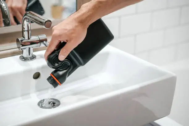 Removal of blockage in the sink, the hand of a man with a bottle of a special remedy with granules. Clean the blockages in the bathroom with chemicals.