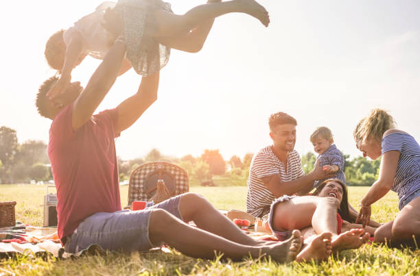 glückliche familien machen picknick im naturpark outdoor - junge eltern spaß mit kindern im sommer gemeinsam lachen - positive stimmung und food konzept - schwerpunkt auf richtige mann gesicht - grass summer day sunset stock-fotos und bilder