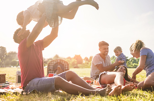 Happy families doing picnic in nature park outdoor - Young parents having fun with children in summer time laughing together - Positive mood and food concept - Main focus on right man face