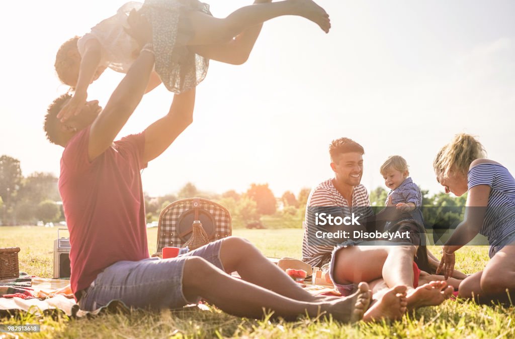 Happy families doing picnic in nature park outdoor - Young parents having fun with children in summer time laughing together - Positive mood and food concept - Main focus on right man face Family Stock Photo