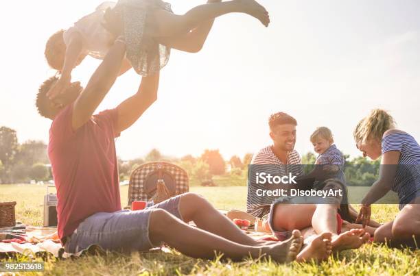 Happy Families Doing Picnic In Nature Park Outdoor Young Parents Having Fun With Children In Summer Time Laughing Together Positive Mood And Food Concept Main Focus On Right Man Face Stock Photo - Download Image Now