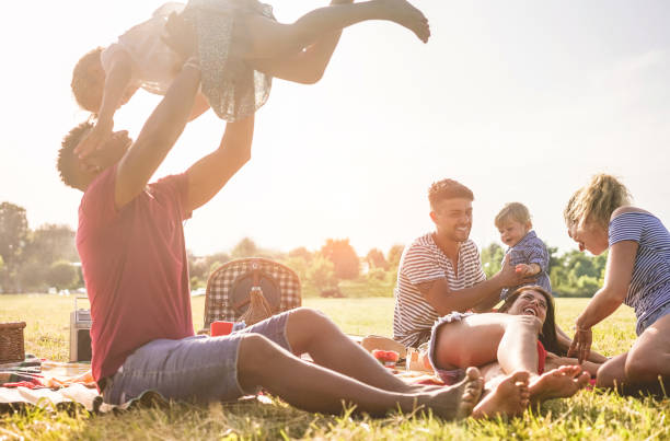 famílias felizes fazendo piquenique no parque natural ao ar livre - pais jovens se divertindo com as crianças no horário de verão, rindo juntos foco de main - conceito positivo de humor e comida - na cara do homem certo - grass summer day sunset - fotografias e filmes do acervo