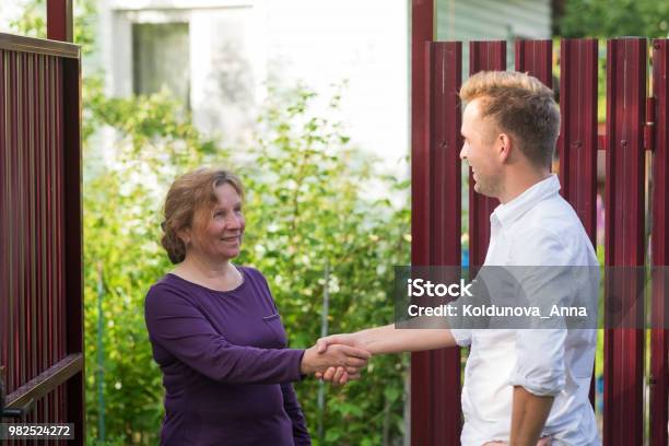 Neighbors Discuss The News Standing At The Fence An Elderly Woman Talking With A Young Man Stock Photo - Download Image Now
