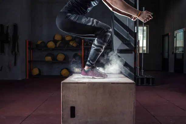 Young woman jumping box and talc powder departs from under feet. Fitness woman doing box jump workout at gym gym.