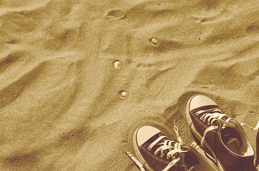 Pair of blue sneakers standing side by side on sand. Summer vacation at sea beach. Retro styled. Copy space.