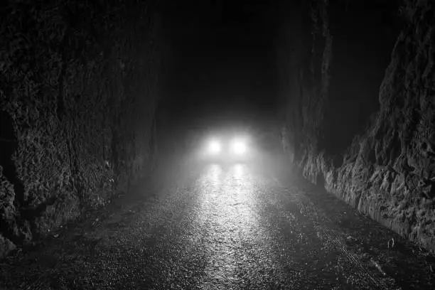 Photo of Black and white scene of Car headlights at night in the foggy road